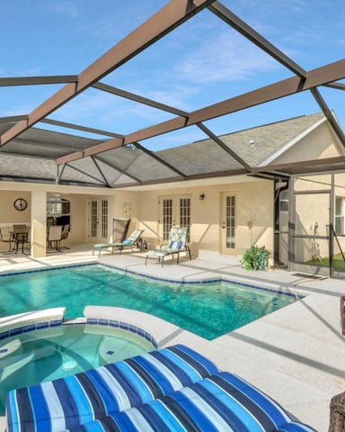 Screened pool enclosure with spa, swimming pool, lounge chairs, and beige house with multiple glass doors