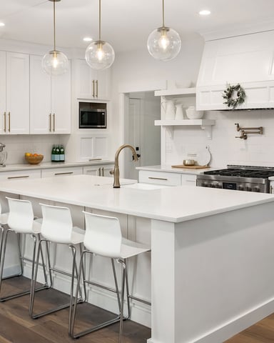Modern white kitchen with stainless steel appliances, large island with white bar seating, pendant lights, and open shelving overlooking deck.