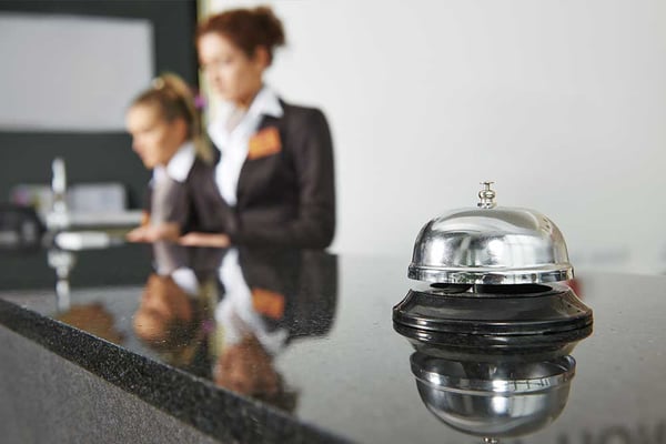 Service bell on hotel reception desk with two staff members in business attire blurred in background